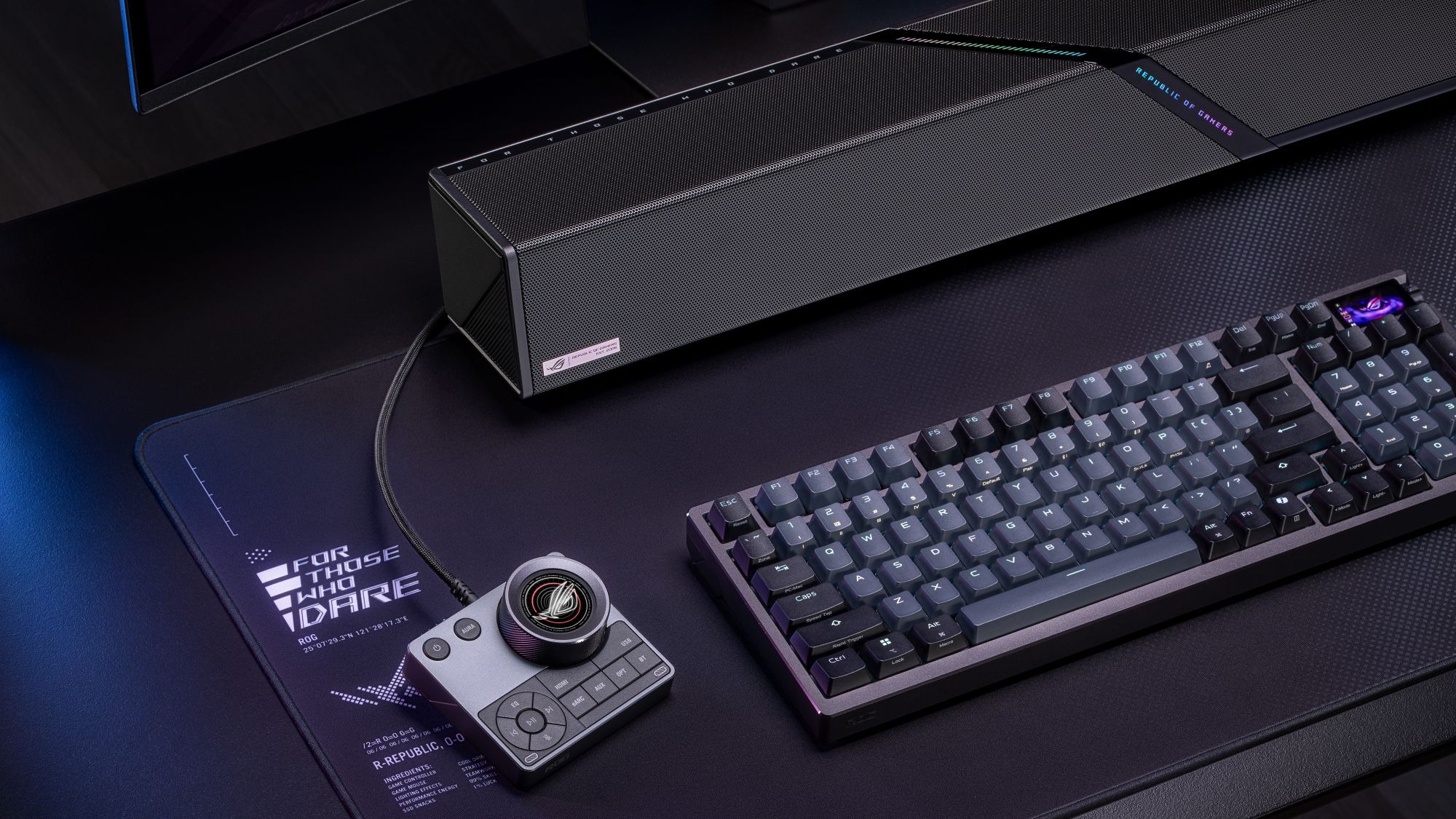 The ROG Gjallar gaming soundbar's control hub positioned beside a keyboard on a black desk.